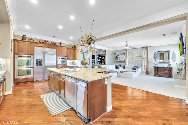 kitchen featuring light wood-type flooring, a kitchen island with sink, stainless steel appliances, sink, and ornamental molding