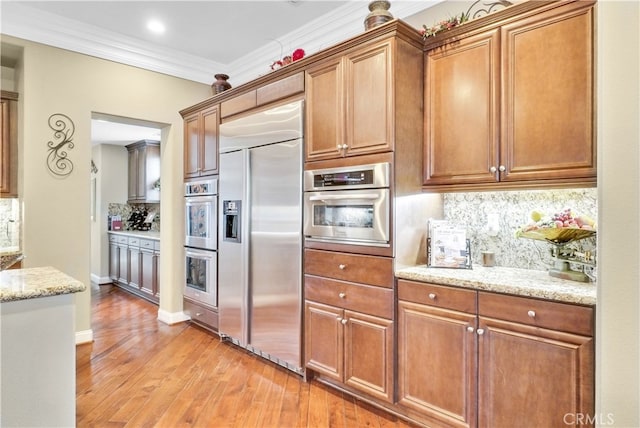 kitchen with tasteful backsplash, crown molding, light hardwood / wood-style flooring, light stone counters, and stainless steel appliances