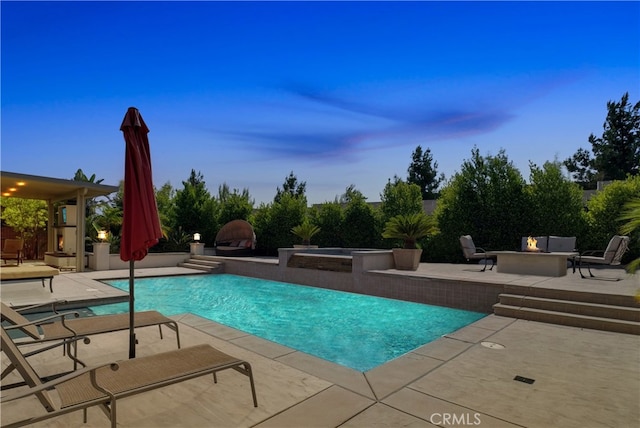 pool at dusk featuring an in ground hot tub and a patio