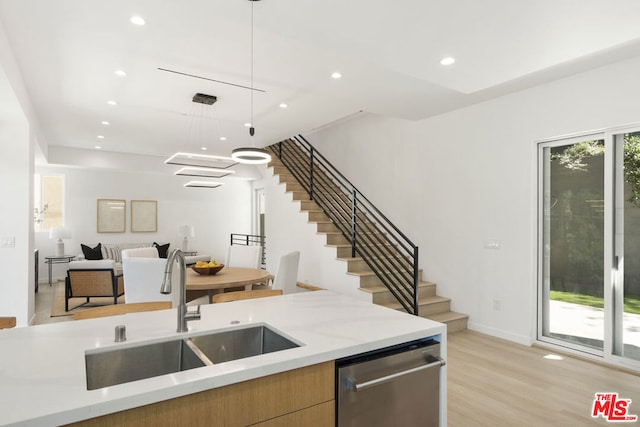 kitchen featuring dishwasher, sink, hanging light fixtures, light stone counters, and light hardwood / wood-style flooring