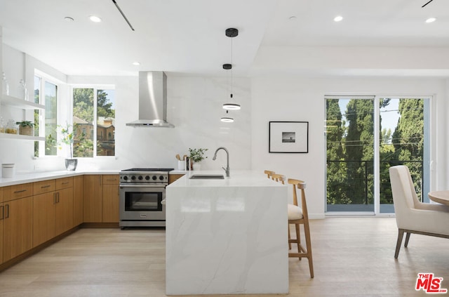 kitchen featuring high end stove, wall chimney exhaust hood, light hardwood / wood-style flooring, sink, and pendant lighting