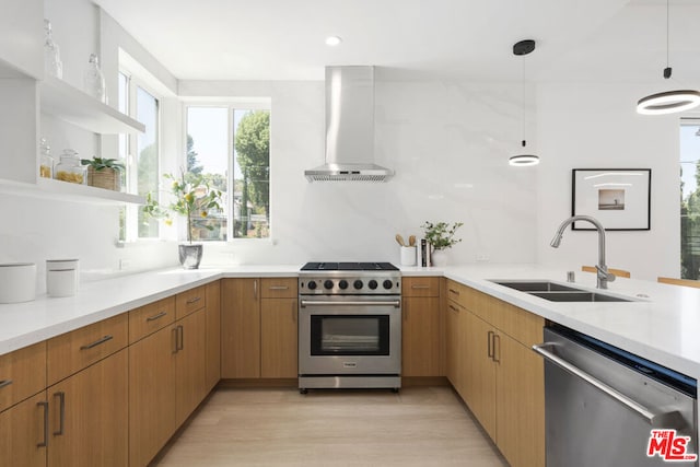 kitchen featuring wall chimney range hood, hanging light fixtures, appliances with stainless steel finishes, light wood-type flooring, and sink