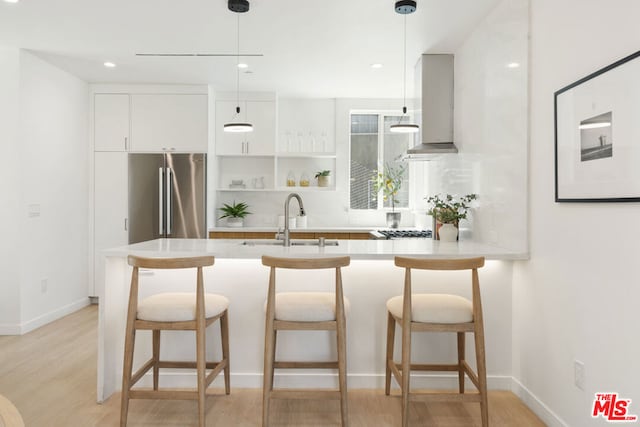 kitchen featuring stainless steel fridge, sink, pendant lighting, light wood-type flooring, and white cabinetry