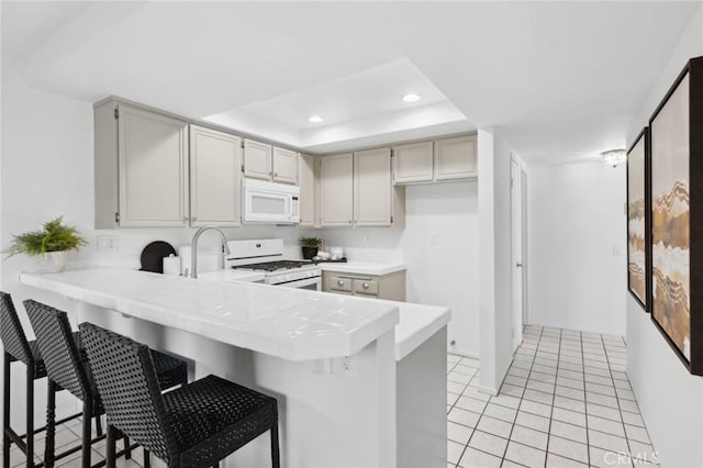 kitchen featuring a breakfast bar, white appliances, a raised ceiling, light tile patterned floors, and kitchen peninsula