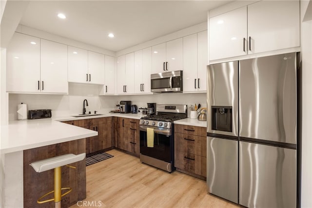 kitchen with sink, stainless steel appliances, light hardwood / wood-style floors, and white cabinetry