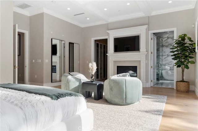 bedroom featuring beam ceiling, light wood-type flooring, ensuite bathroom, and crown molding