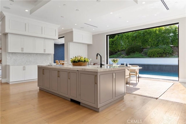 kitchen featuring a center island with sink, white cabinets, ornamental molding, and light wood-type flooring