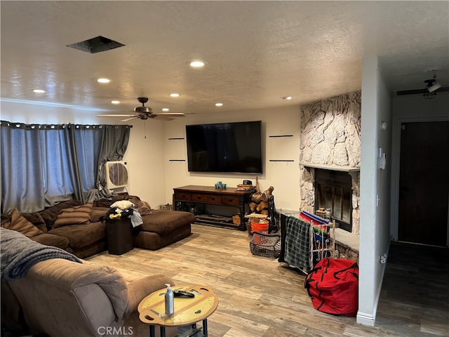 living room with light hardwood / wood-style flooring, a stone fireplace, a textured ceiling, and ceiling fan