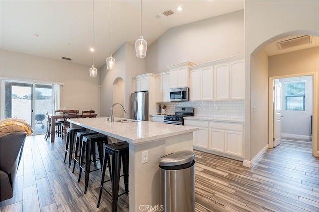 kitchen with hanging light fixtures, appliances with stainless steel finishes, a kitchen island with sink, and white cabinets