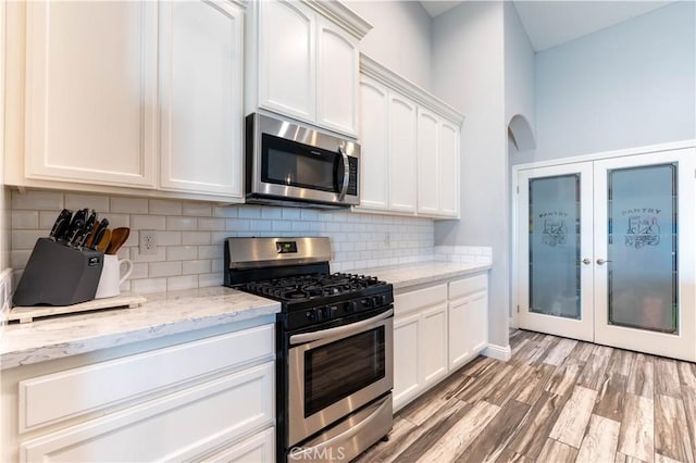 kitchen featuring light hardwood / wood-style flooring, stainless steel appliances, light stone counters, white cabinets, and decorative backsplash