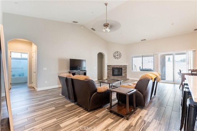 living room with lofted ceiling, a stone fireplace, light hardwood / wood-style flooring, and ceiling fan