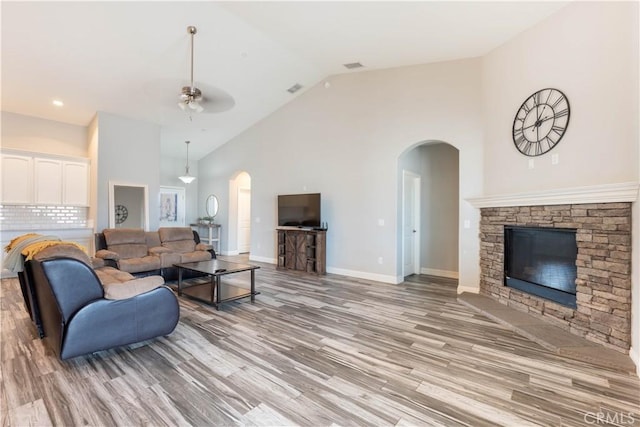 living room featuring ceiling fan, high vaulted ceiling, a fireplace, and light hardwood / wood-style floors