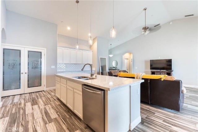 kitchen with white cabinetry, dishwasher, sink, light stone counters, and a center island with sink