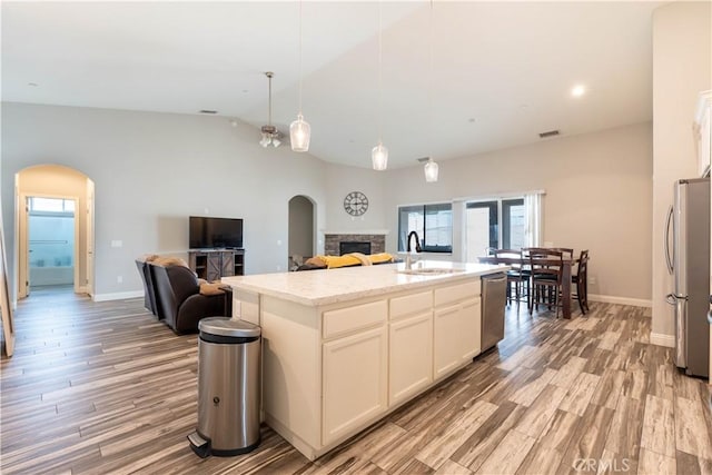 kitchen with sink, stainless steel appliances, light stone countertops, a center island with sink, and decorative light fixtures