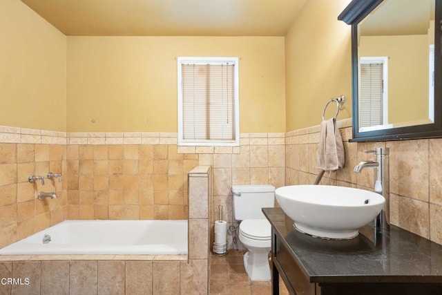 bathroom featuring tile patterned floors, tiled bath, toilet, vanity, and tile walls