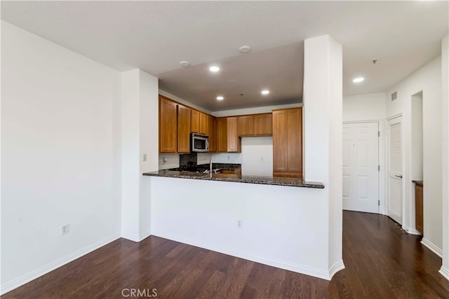 kitchen with dark stone counters, dark wood-type flooring, and kitchen peninsula