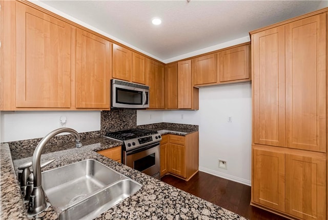 kitchen with dark stone countertops, sink, stainless steel appliances, and dark hardwood / wood-style flooring