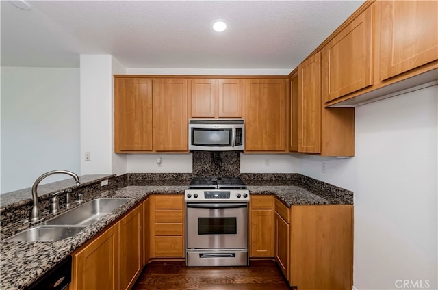 kitchen with a textured ceiling, dark wood-type flooring, sink, stainless steel appliances, and dark stone countertops