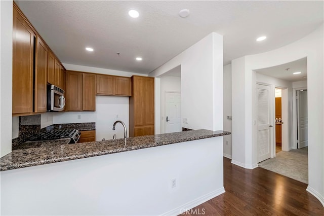 kitchen featuring dark stone countertops, appliances with stainless steel finishes, kitchen peninsula, and dark hardwood / wood-style flooring