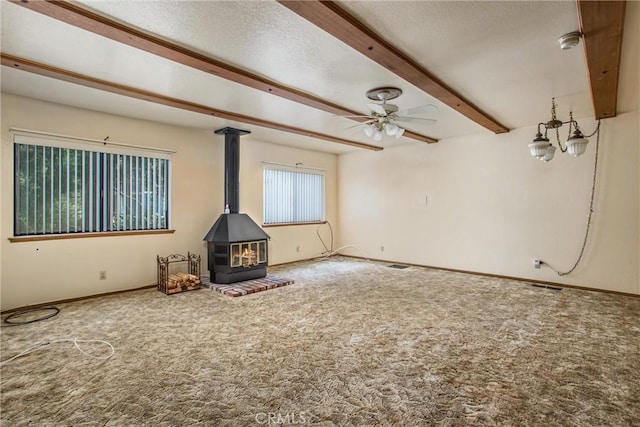 unfurnished living room featuring a textured ceiling, ceiling fan, beamed ceiling, carpet floors, and a wood stove