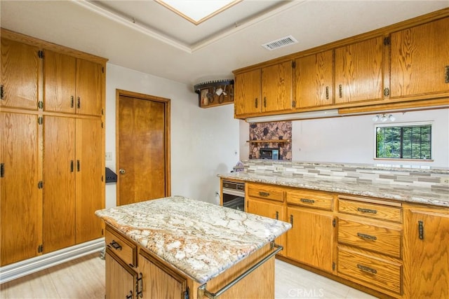 kitchen with decorative backsplash, a center island, light stone counters, and light hardwood / wood-style flooring