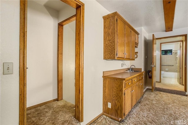 hallway featuring beamed ceiling, light colored carpet, and sink