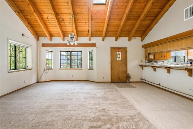 unfurnished living room with a skylight, beamed ceiling, light colored carpet, wood ceiling, and a chandelier