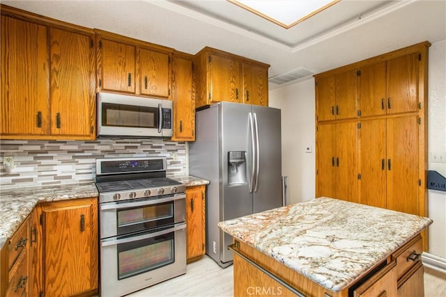 kitchen with decorative backsplash, stainless steel appliances, light stone counters, and light wood-type flooring