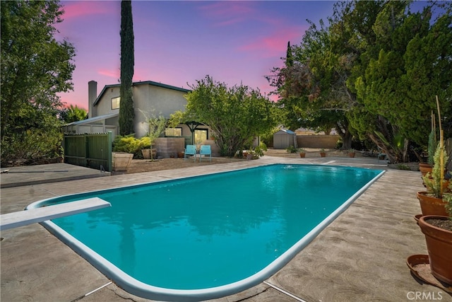 pool at dusk featuring a diving board and a patio area