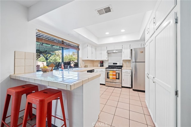 kitchen featuring kitchen peninsula, white cabinetry, stainless steel appliances, tile countertops, and a kitchen breakfast bar