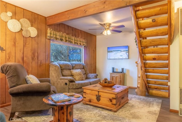 living area with beam ceiling, a ceiling fan, wood finished floors, wooden walls, and baseboards