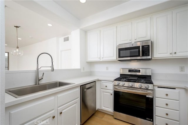 kitchen featuring appliances with stainless steel finishes, white cabinets, hanging light fixtures, and sink