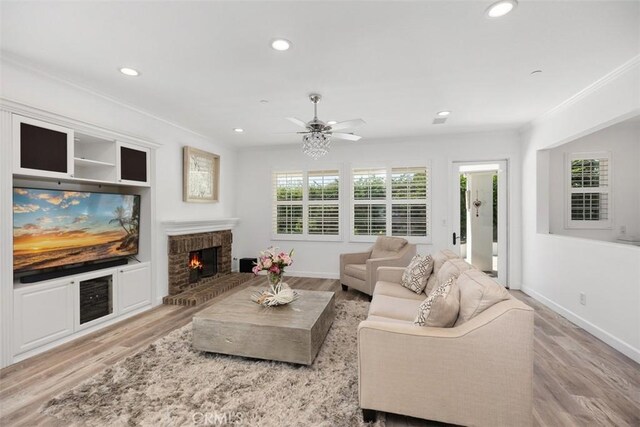 living room with ceiling fan, light wood-type flooring, a brick fireplace, and crown molding