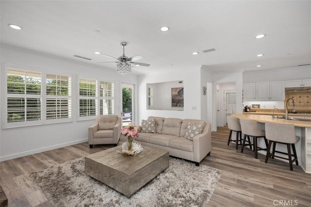 living room with ceiling fan, sink, and light wood-type flooring