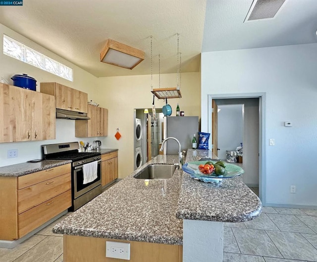 kitchen with stacked washing maching and dryer, an island with sink, stainless steel range with gas stovetop, and sink