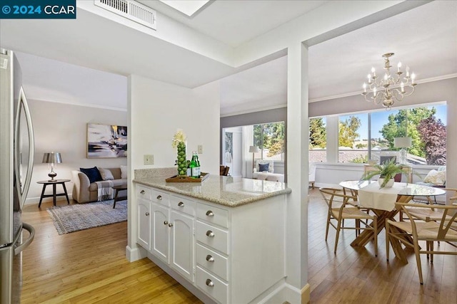 kitchen with white cabinetry, stainless steel refrigerator, light hardwood / wood-style flooring, a notable chandelier, and light stone counters