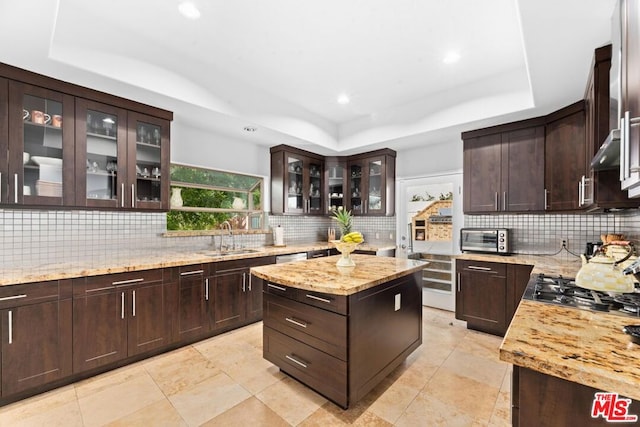 kitchen with dark brown cabinetry, a center island, sink, light stone counters, and a tray ceiling