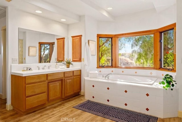 bathroom with vanity, wood-type flooring, and a relaxing tiled tub