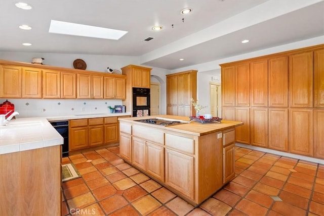 kitchen featuring tile counters, sink, a center island, lofted ceiling with skylight, and stainless steel gas stovetop