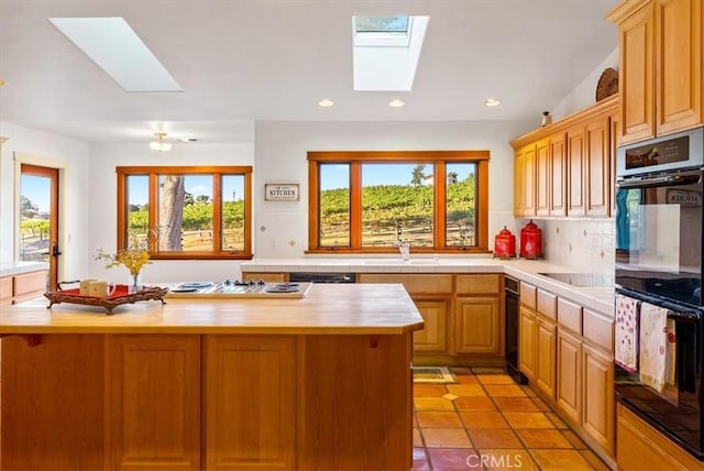 kitchen with light brown cabinets, a skylight, tasteful backsplash, and black appliances