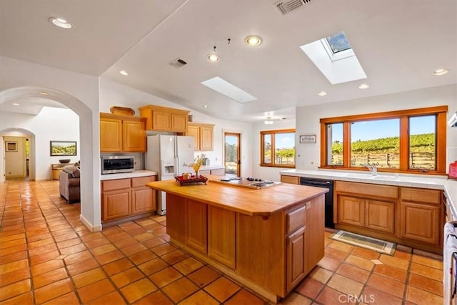 kitchen featuring butcher block counters, sink, stainless steel appliances, vaulted ceiling with skylight, and a kitchen island