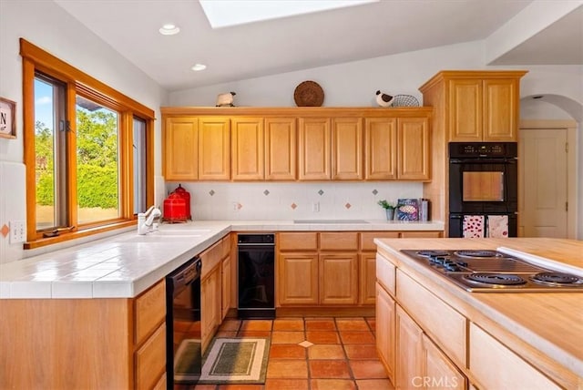 kitchen with lofted ceiling with skylight, black appliances, sink, decorative backsplash, and light tile patterned flooring