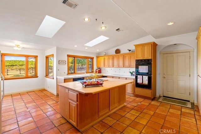 kitchen with a center island, light tile patterned floors, black appliances, and vaulted ceiling with skylight