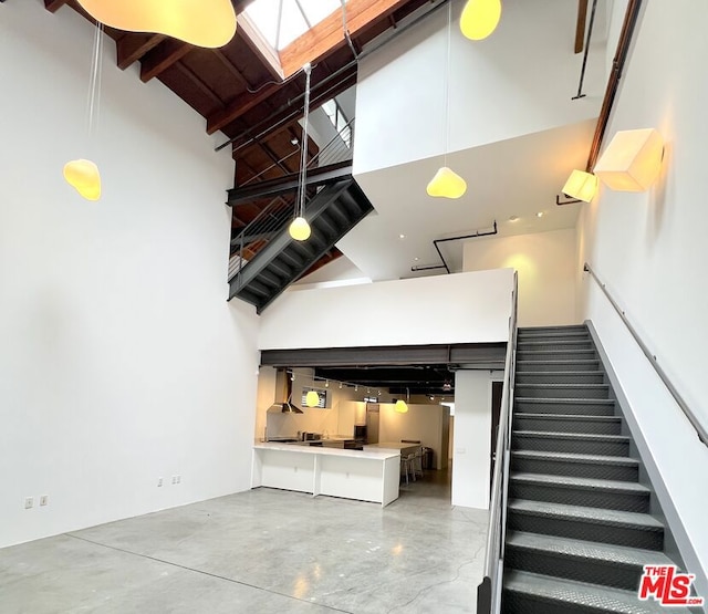 staircase with concrete flooring, a skylight, high vaulted ceiling, and beam ceiling