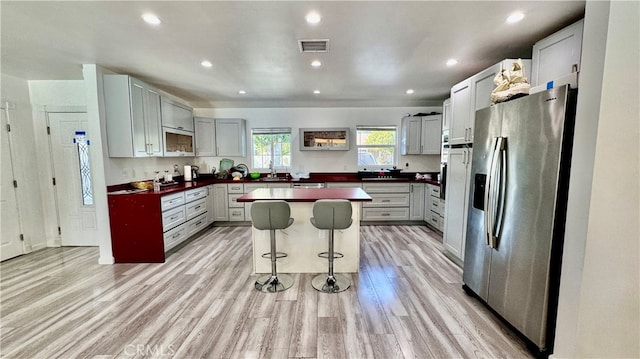 kitchen with light wood-type flooring, a kitchen island, a breakfast bar, sink, and stainless steel refrigerator with ice dispenser