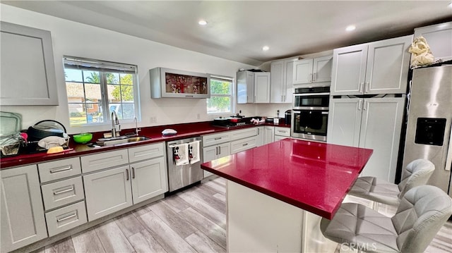 kitchen with sink, light hardwood / wood-style flooring, stainless steel appliances, a center island, and a kitchen bar