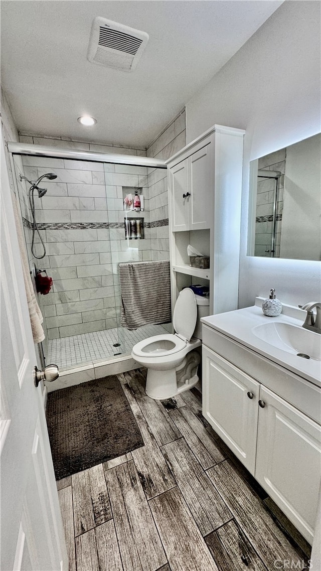 bathroom with a shower with door, vanity, hardwood / wood-style floors, and toilet