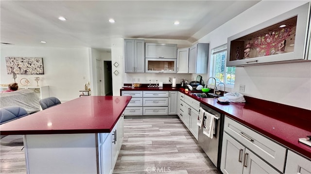 kitchen with gray cabinetry, light wood-type flooring, a breakfast bar, sink, and stainless steel dishwasher