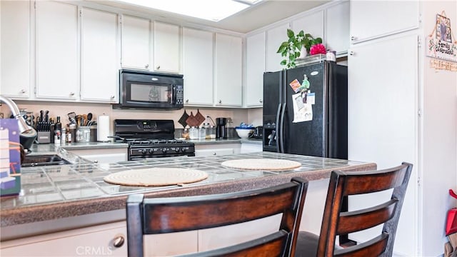 kitchen featuring a peninsula, black appliances, a breakfast bar area, and white cabinets