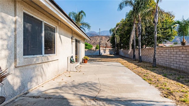 view of side of home with a fenced backyard, a mountain view, a patio, and stucco siding